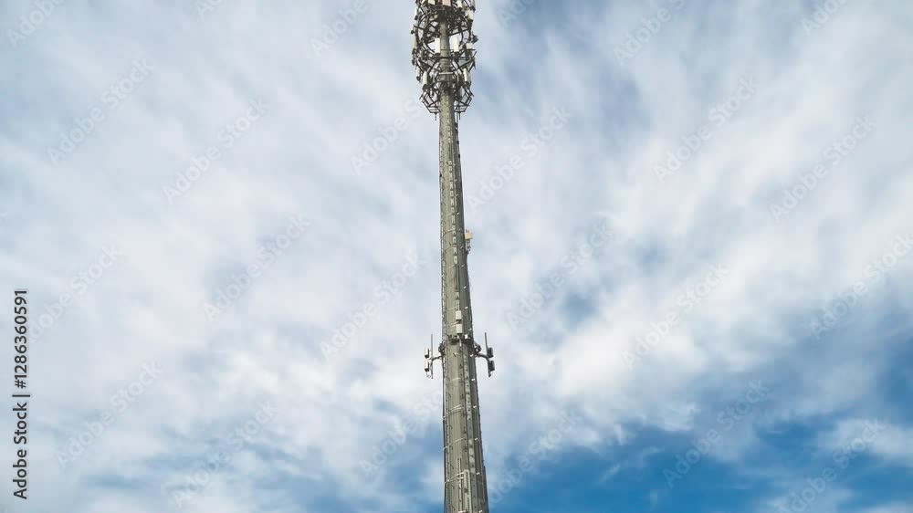 Tilting downward shot to the ground of a cellular communications tower and antenna on a sunny day with moving clouds. Tilting downward shot to the ground of a cellular communications tower and antenna on a sunny day with moving clouds.