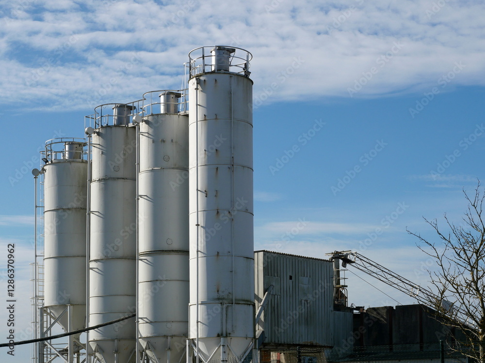 Multiple silos of a concrete plant rise into the sky. Industrial facility in a commercial area, essential for building materials. A technical and architectural motif. Multiple silos of a concrete plant rise into the sky. Industrial facility in a commercial area, essential for building materials. A technical and architectural motif.
