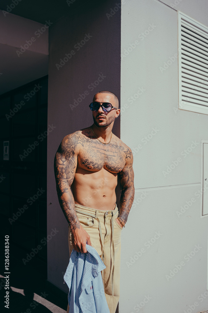 Chico joven tatuado posando con ropa actual en la calle