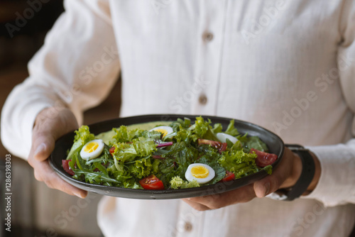 Close-up of a man holding a bowl of salad with eggs and cherry tomatoes. Waiter