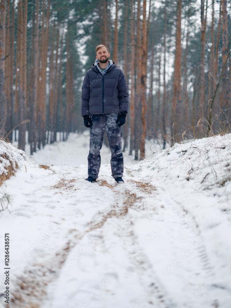 Naklejka premium Happy young smiling man walking on wood dirt road in snowy forest.