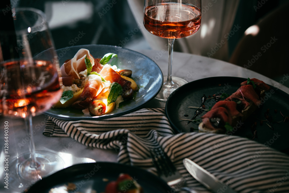 A table served for a dinner with prosciutto salad and rose wine in a bar or restaurant.