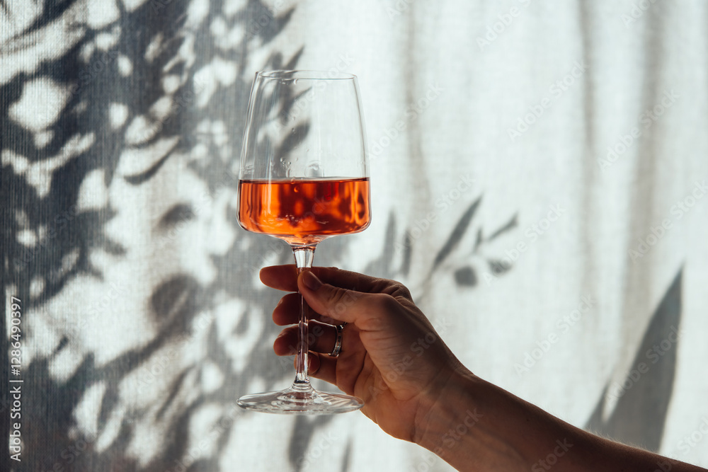 Hand holding a glass of rose wine in summer sunshine during a wine tasting in a bar or restaurant.