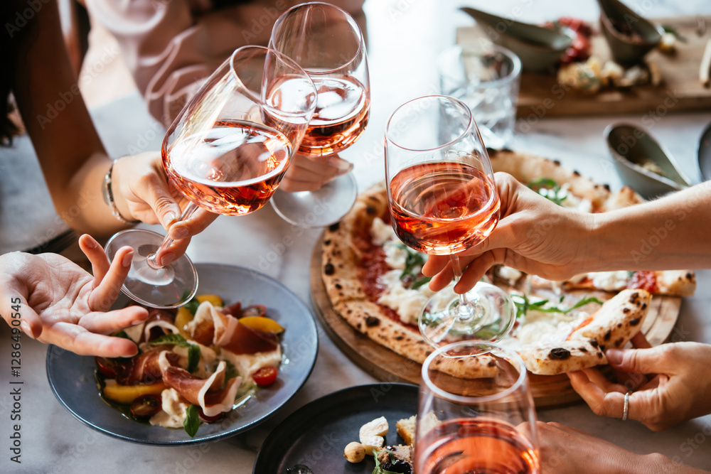 Friends enjoy a dinner party with pizza and rose wine in a bar or a restaurant.