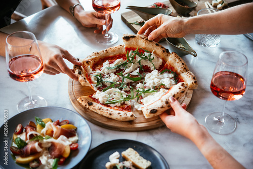 Friends enjoy a dinner party with pizza and rose wine in a bar or a restaurant.