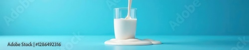 Gentle pour of milk into a glass on a blue background spills onto the table, glass, blue