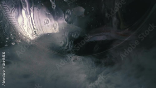 Swirling water and soap inside washing machine.
Close-up view of inside of a washing machine during a wash cycle. The scene captures the motion of water, soap suds, and some fabric being agitated. 