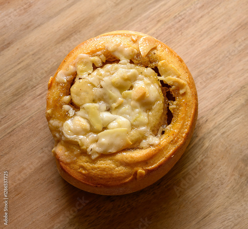 A delicious tosca roll sits on a wooden surface, generously drizzled with creamy icing. The warm pastry invites indulgence with its sweet aroma