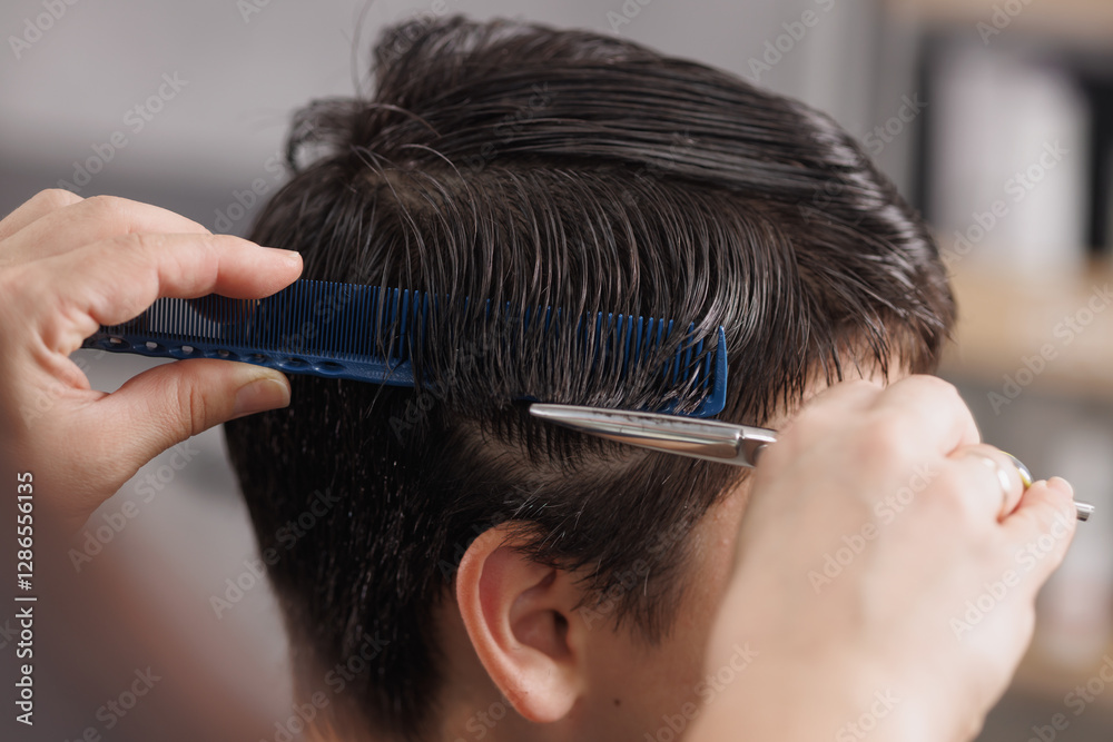 Fototapeta premium Close-up of a professional hairstylist cutting wet hair with scissors and a comb in a modern salon, ensuring precision and style.