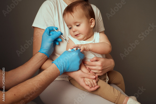 A healthcare provider gives a vaccination to a young child seated on a mother's lap. The provider wears blue gloves, ensuring a safe inoculation process. The setting is calm and clinical