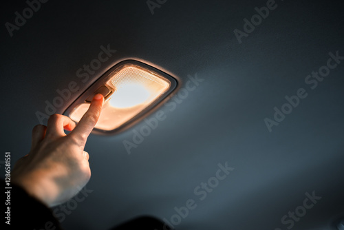 Obraz na plátně A person's hand reaches towards a car's overhead light on the ceiling