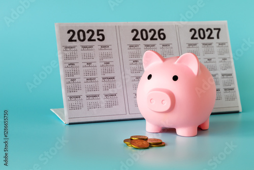 A piggy bank in the form of a pink pig, a desktop calendar for 2025-2027 and a pile of coins on a light blue background. The concept of long-term investments.