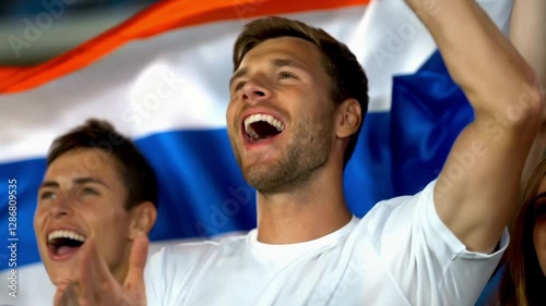 Fans celebrating and waving Netherlands flag at a sports event
