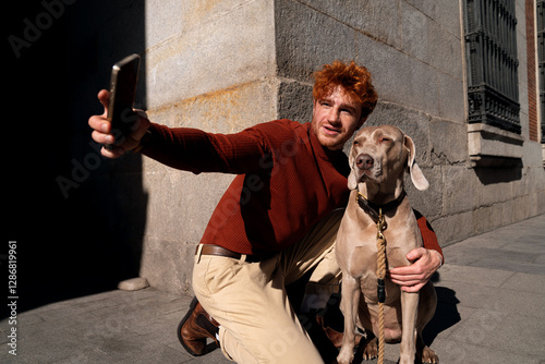Young ginger haired boy taking a happy selfie with his pet dog on the street