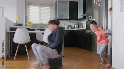 Two kids are enthusiastically running and playing indoors, engaging in fun activities. They exhibit joy and excitement in a modern kitchen setting, creating a lively atmosphere.