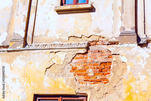 Obraz na płótnie Section of an old deteriorating building facade with visible damage. Plaster has fallen off in several areas, revealing underlying red brickwork and some decorative elements near top of the wall w salonie