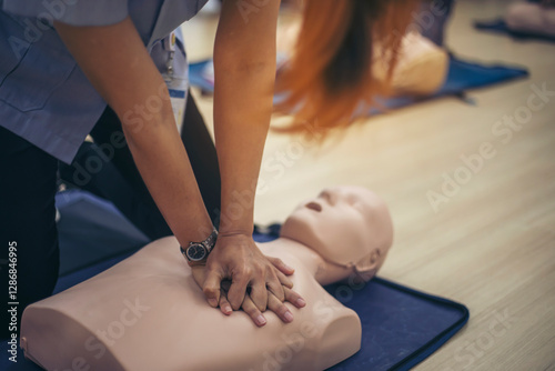 Close-up of Asian hands practicing cardiopulmonary resuscitation (CPR) on a training dummy. Important techniques include chest compressions and maintaining an airway.