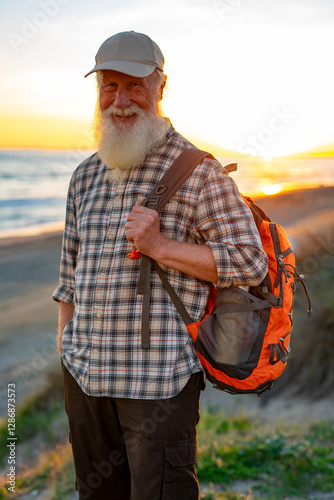 Smiling Elderly Man with Long White Beard and Backpack Enjoying Coastal Sunset photo