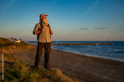 Senior Man with Long White Beard Hiking Along Coastal Cliffs at Sunset photo