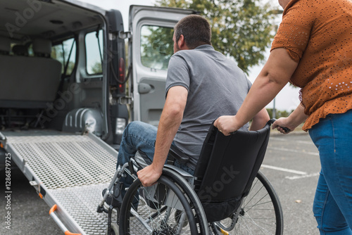 Female assistant pushing a man with disability, a wheelchair user up the car ramp into the van. Accessibility and travel concepts.