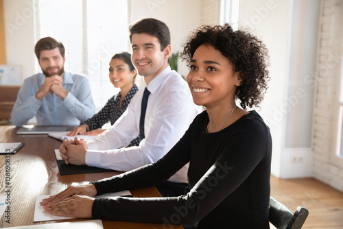 African, European, Indian teammates attend briefing, seminar or training event listening attentively to speaker, seated at conference table, gaining skills, new knowledge during professional workshop