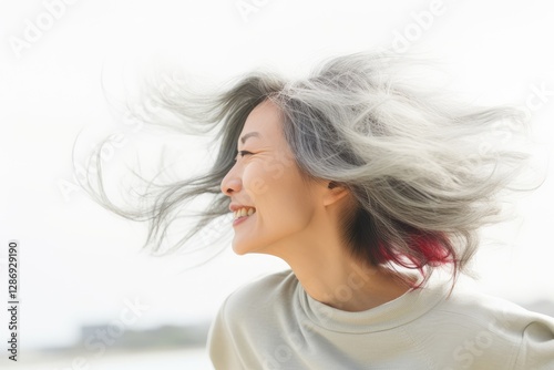 Asian woman with flying silver hair smiling in sunlight. Natural beauty and freedom concept, emotional portrait with wind effect and bright backlight