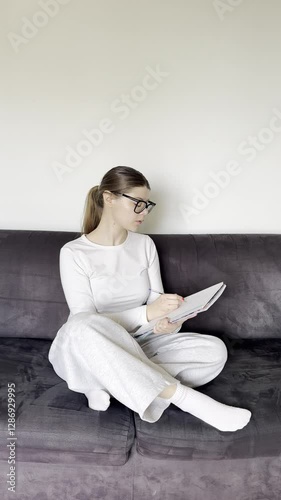 A young woman writes in her notebook, planning, setting goals. Focused and engaged, self-improvement, motivation, personal development. Tracking progress, organised, working or studying from home