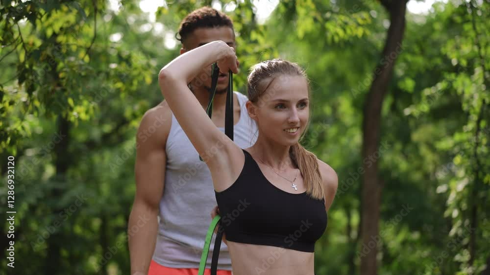 A yoga trainer with dreads assists a young woman with a stretching exercise in a park. She is smiling and receiving support from the trainer, who is guiding her through the stretch. The scene is set A yoga trainer with dreads assists a young woman with a stretching exercise in a park. She is smiling and receiving support from the trainer, who is guiding her through the stretch. The scene is set