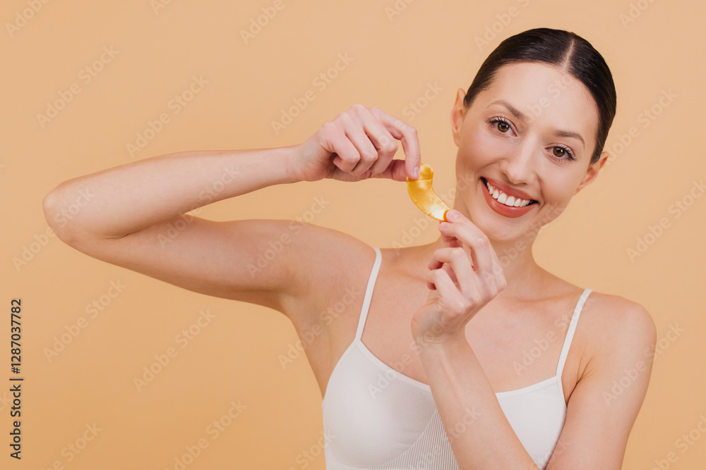 Smiling Woman Holding Golden Eye Patches for Skin Care Treatment on Beige Background Smiling Woman Holding Golden Eye Patches for Skin Care Treatment on Beige Background