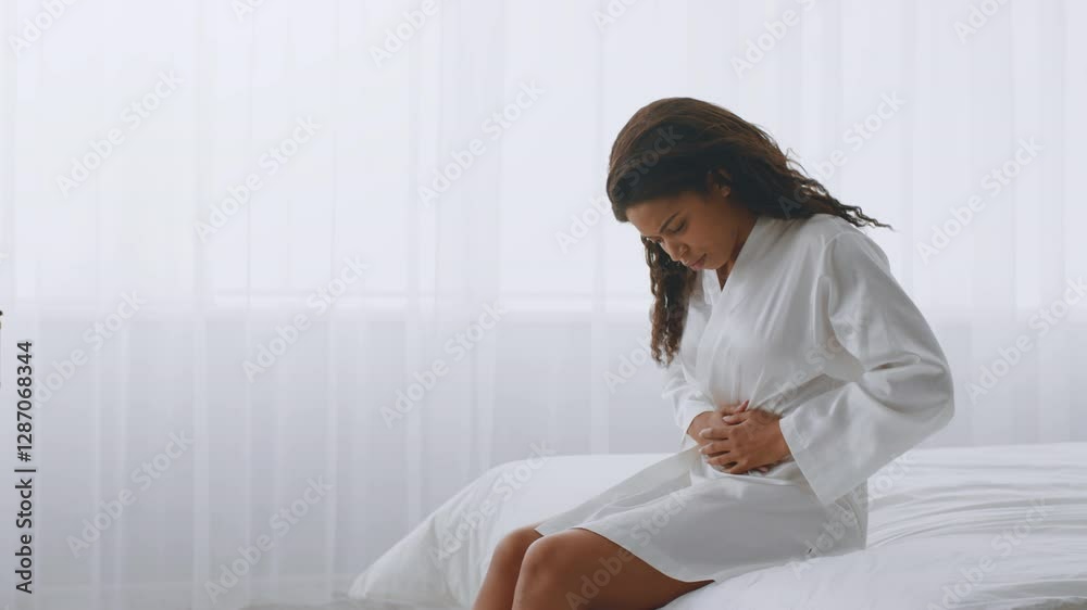 A millennial woman sits on her bed in a cozy bedroom, wearing a bathrobe and reflecting quietly. Soft light filters through sheer curtains, creating a serene atmosphere, copy space A millennial woman sits on her bed in a cozy bedroom, wearing a bathrobe and reflecting quietly. Soft light filters through sheer curtains, creating a serene atmosphere, copy space