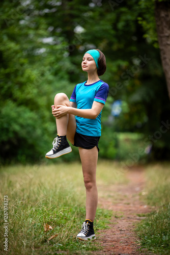 Beautiful teen girl in sports clothes doing sports outdoors in park in summer