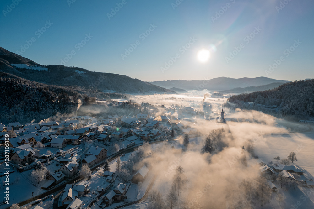 Beautiful village of Ljubno ob Savinji in cold winter morning. Visible haze from the river, sun rising up and smoke coming out of smokestacks.