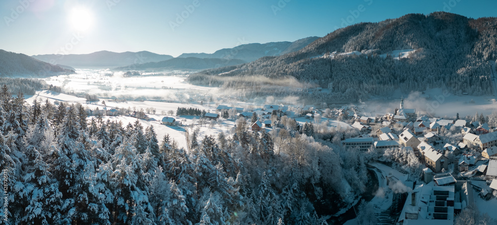 Beautiful village of Ljubno ob Savinji in cold winter morning. Visible haze from the river, sun rising up and smoke coming out of smokestacks.
