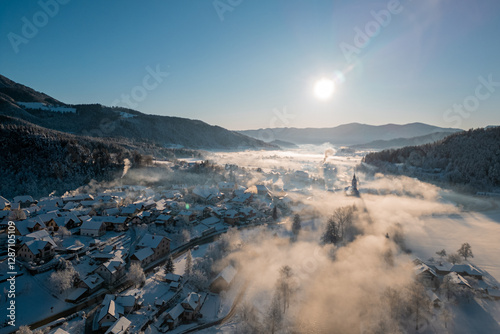 Obraz na płótnie Beautiful village of Ljubno ob Savinji in cold winter morning. Visible haze from the river, sun rising up and smoke coming out of smokestacks. w salonie