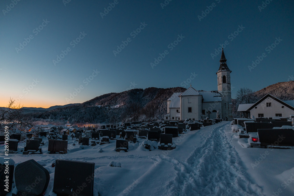 Beautiful church at Ljubno ob Savinji in cold winter morning. Visible haze from the river, sun rising up and smoke coming out of smokestacks.