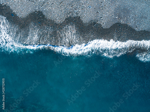 Colorful waves gently wash up on a rocky shore under clear blue skies in a coastal setting