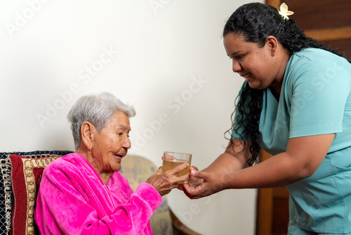 Nurse giving glass of water to elderly woman at home