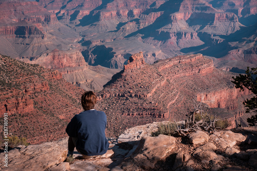 A man from behind seated on Grand Canyon cliff, Grand Canyon in the background