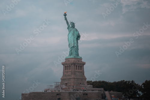 Distant view of the Statue of Liberty on Liberty Island, New York City, with a cloudy sky.