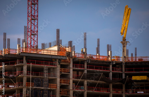 A far shot of a construction worker on the top of a building with rebar and a cement pump