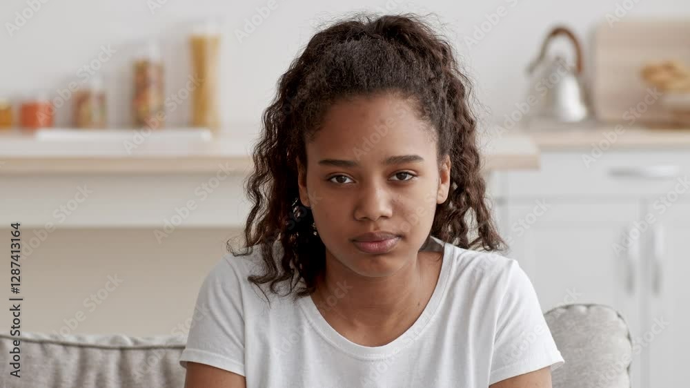 A teenage girl sits alone on a couch in her cozy living room, deep in thought. The bright space features a coffee table and shelves with various items, capturing a moment of reflection. A teenage girl sits alone on a couch in her cozy living room, deep in thought. The bright space features a coffee table and shelves with various items, capturing a moment of reflection.