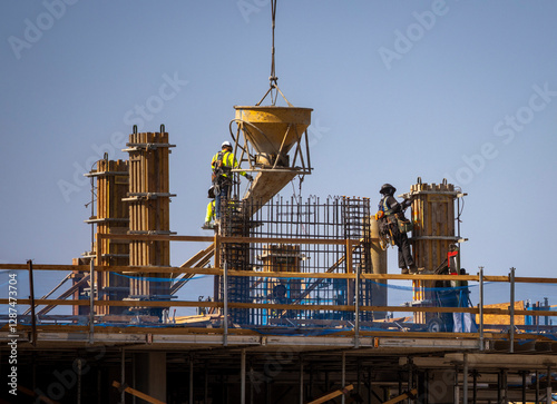 Construction workers guiding a large cement bucket held by a crane at a commercial construction site