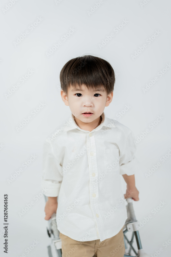 young boy in white shirt stands against plain background, holding walker young boy in white shirt stands against plain background, holding walker