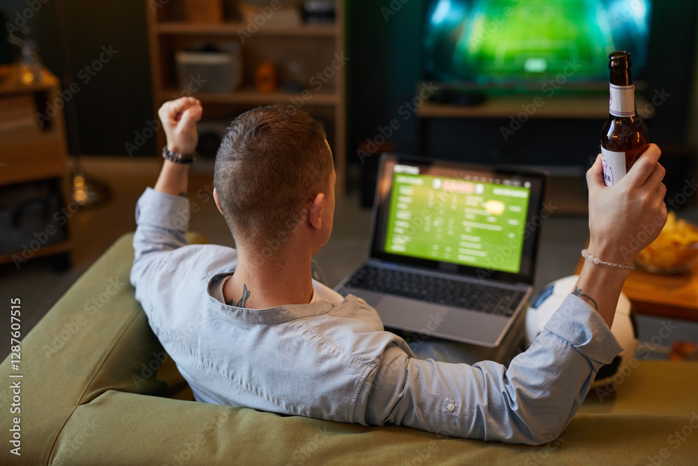 Person sitting on couch watching soccer game on laptop, with hand holding beer bottle, providing a casual and relaxed atmosphere Person sitting on couch watching soccer game on laptop, with hand holding beer bottle, providing a casual and relaxed atmosphere