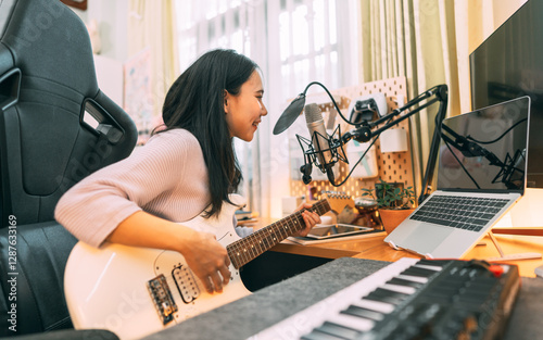 Young asian woman composer playing guitar music with digital technology at home studio