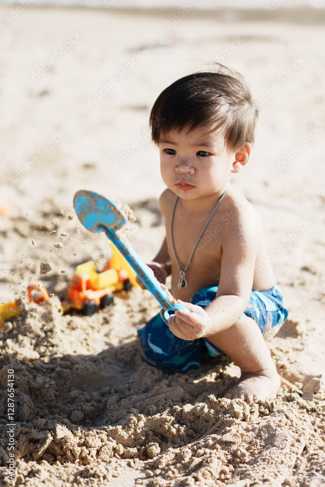 young child plays joyfully in sand at beach, using blue shovel to dig and build. sunny day adds warmth to scene, with toy truck visible in background young child plays joyfully in sand at beach, using blue shovel to dig and build. sunny day adds warmth to scene, with toy truck visible in background