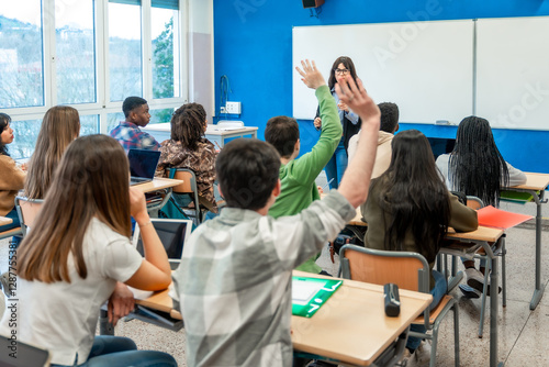 High school students raising hands in classroom during lesson photo