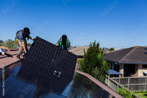 Team of workmen laying all Black bifacial solar panels on roof