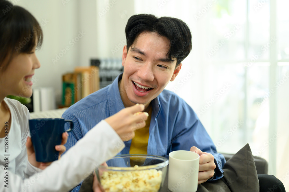 Happy young couple sitting on the couch, sharing a bowl of popcorn while watching movie Happy young couple sitting on the couch, sharing a bowl of popcorn while watching movie