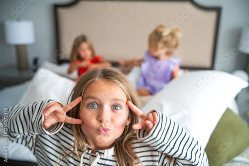 Young Girl making Peace Sign and Duck Lips while Sisters Play in Bed photo